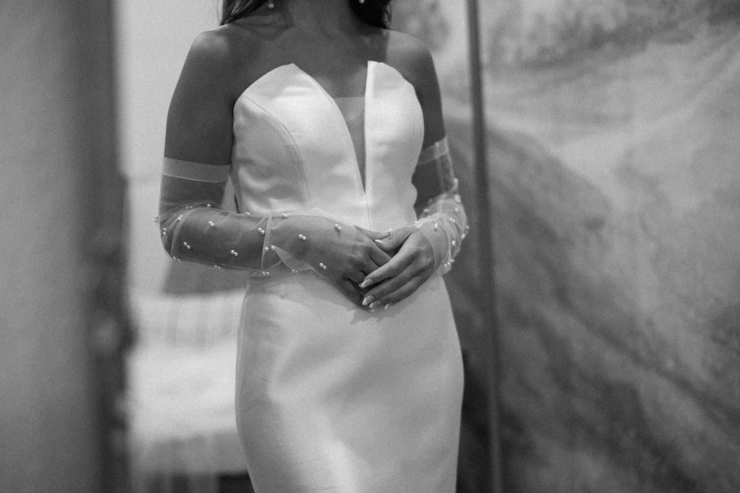 A black and white wedding photo showing a bride in a sleeveless gown standing against a textured background.