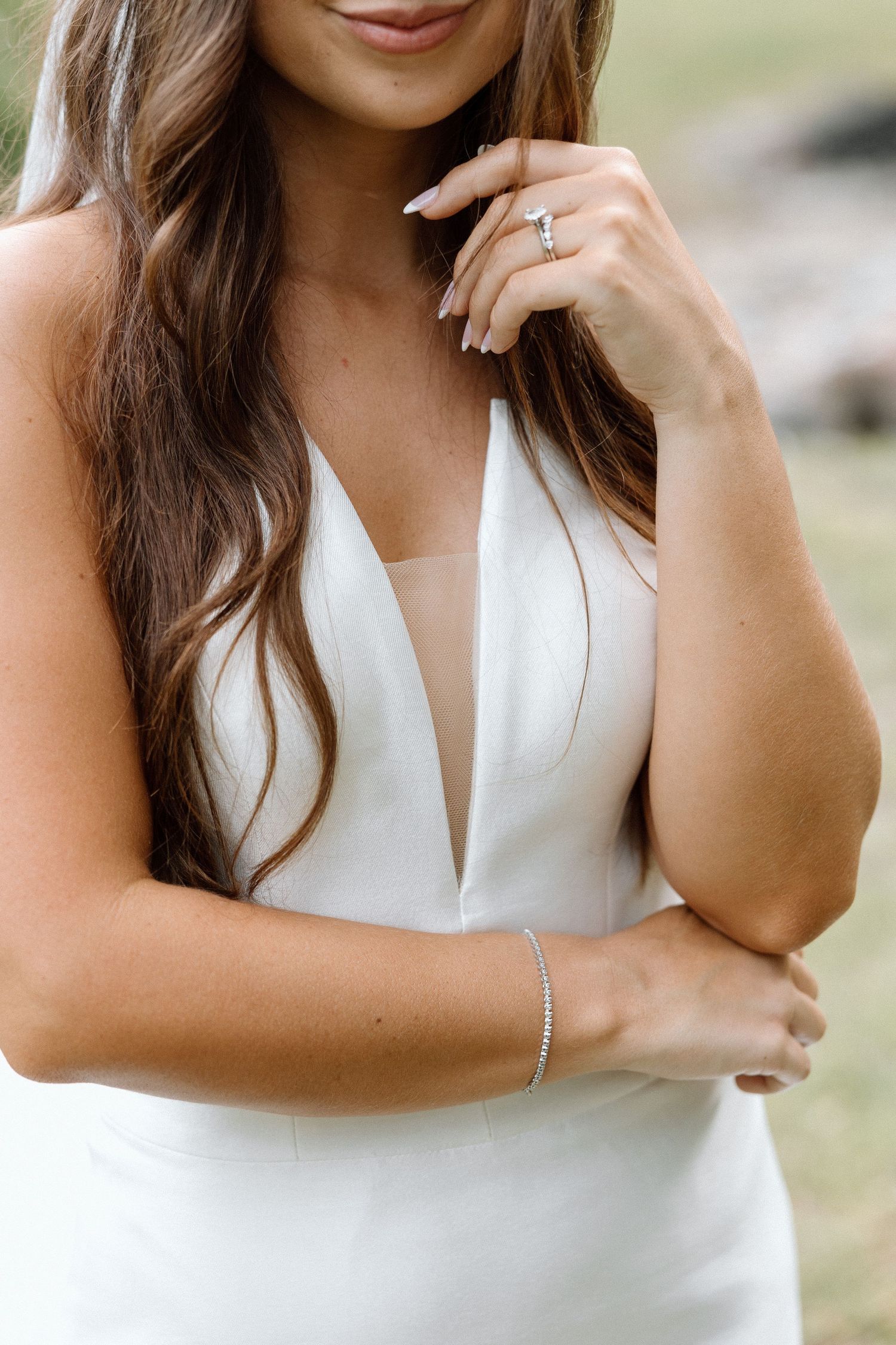 Close-up detail of a bride in a white plunging neckline wedding dress with long wavy hair and delicate bracelet.