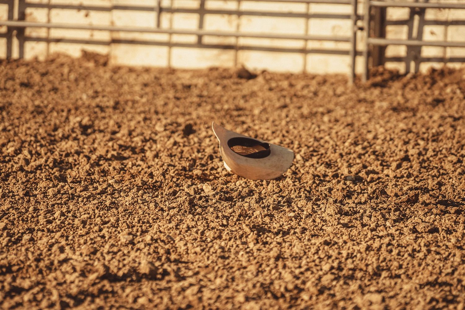 A lone white cowboy hat rests in the dirt of a rodeo arena after being thrown from a rider.