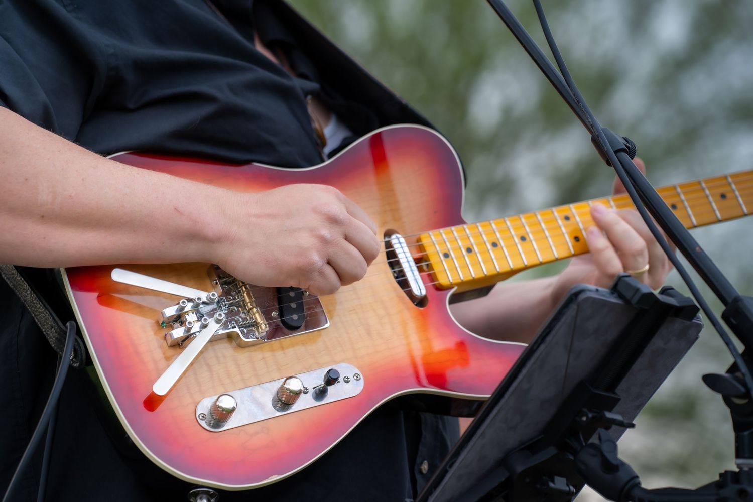 Close-up of hands playing sunburst Fender Telecaster electric guitar at outdoor concert.