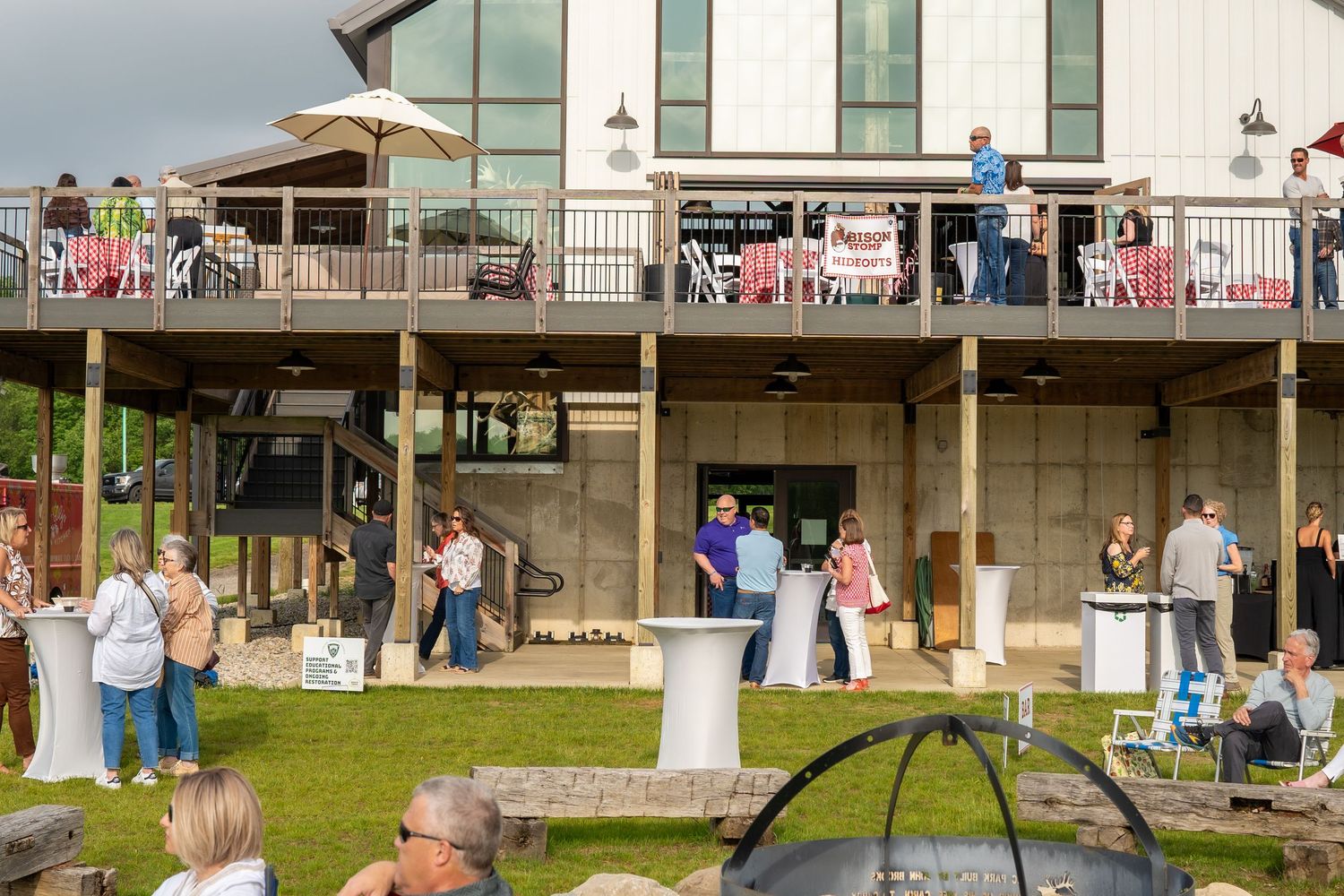 Guests mingling on a large deck and lawn area of a modern farmhouse venue during an outdoor evening event.