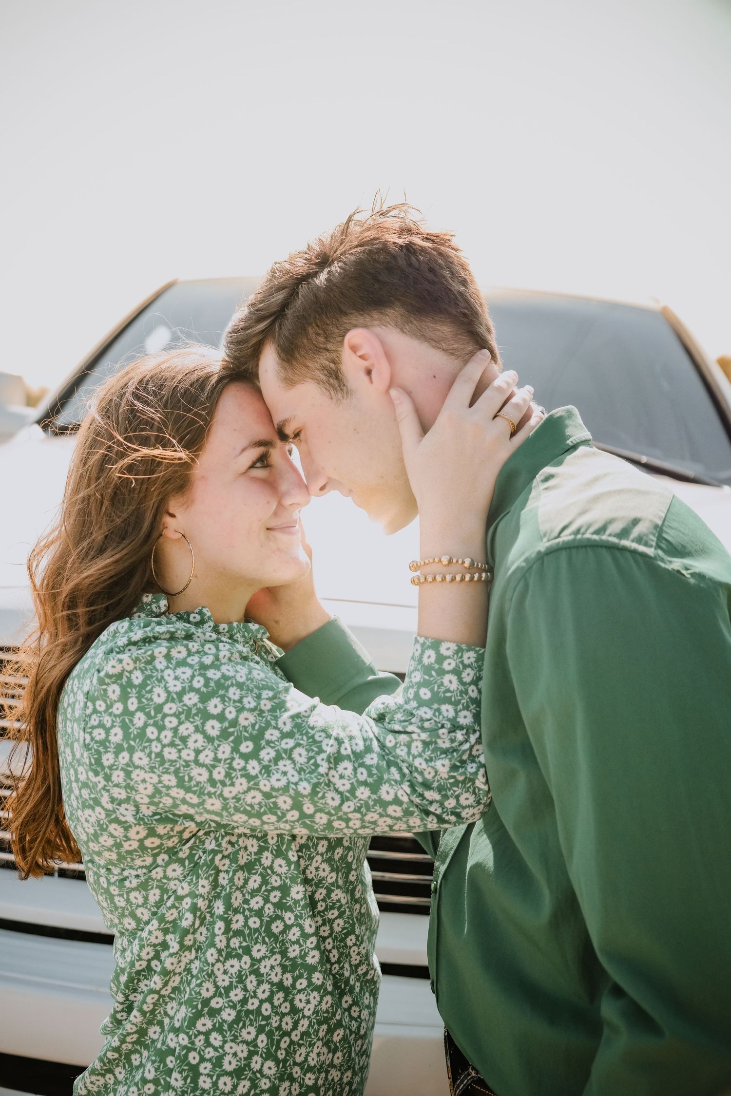 Romantic couple in matching green outfits touching foreheads tenderly in front of a white truck outdoors.