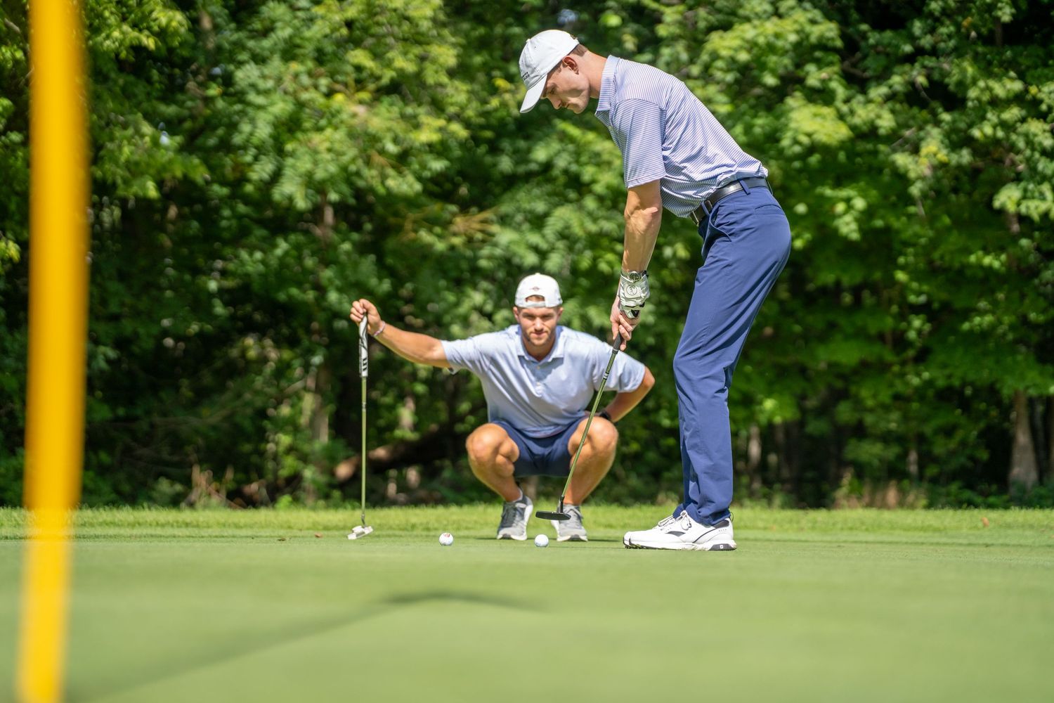 Two golfers reading a putt on a lush green golf course surrounded by trees.