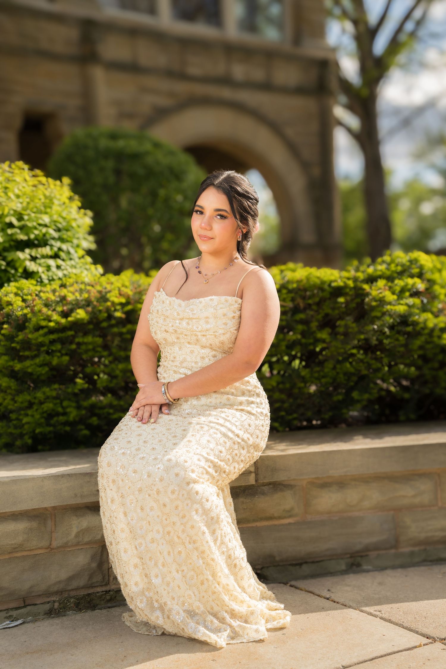 Young woman in floral maxi dress seated on stone steps outside historic building.