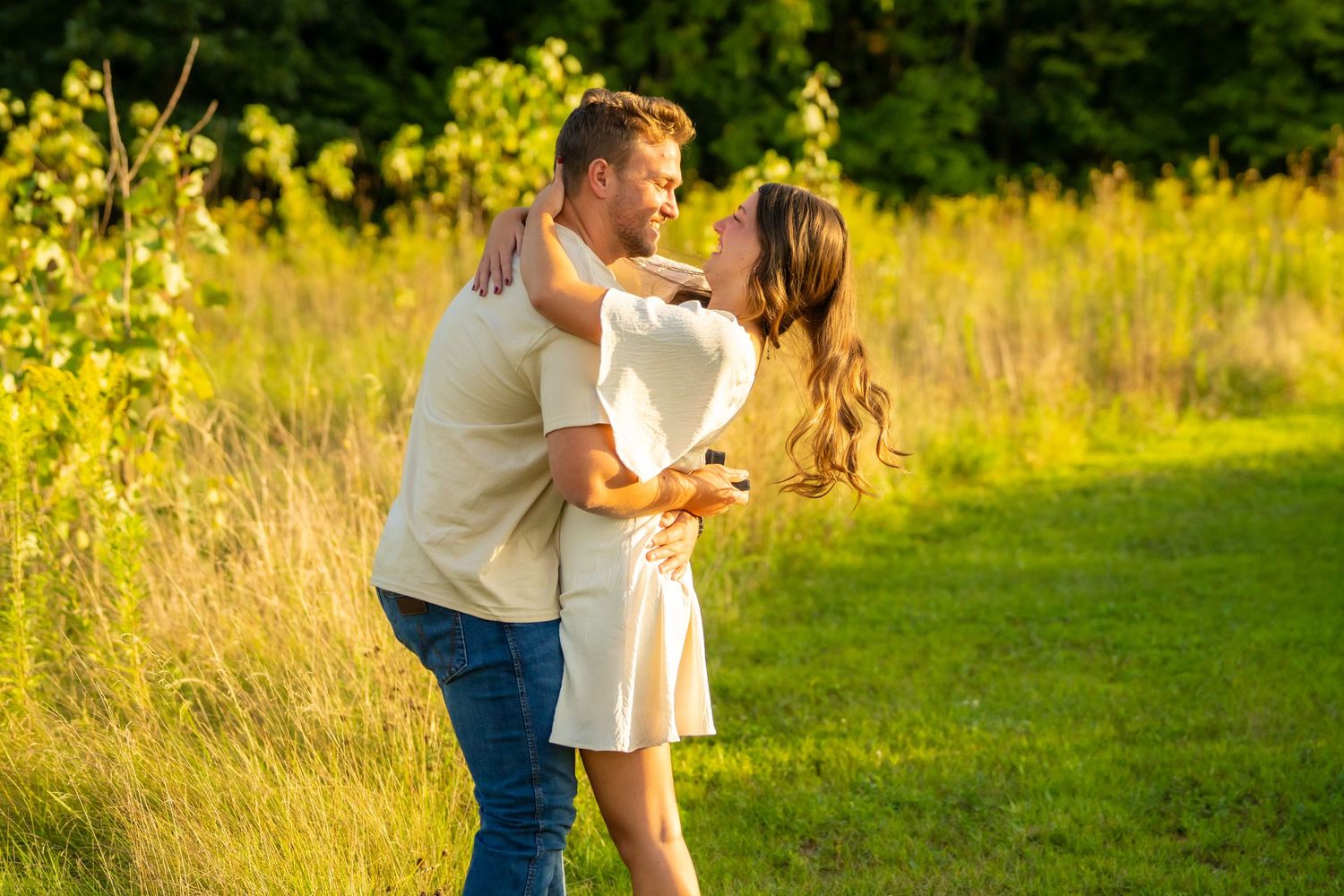 Happy couple embracing and nearly kissing in a golden sunlit meadow after an engagement.