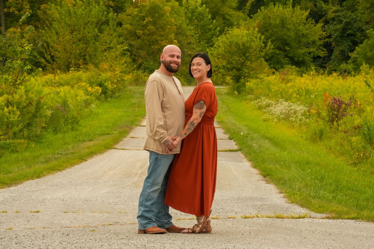 Couple holding hands smiling on a gravel path surrounded by lush green and yellow foliage.