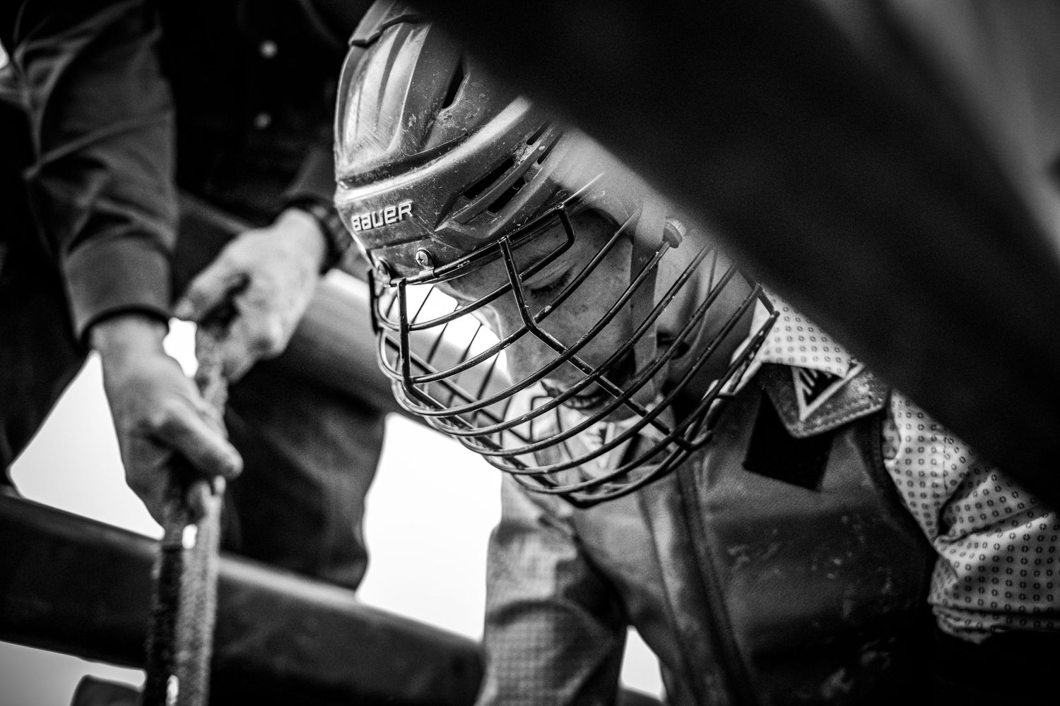 Black and white close-up of a hockey player wearing a cage helmet and holding a stick on the ice.