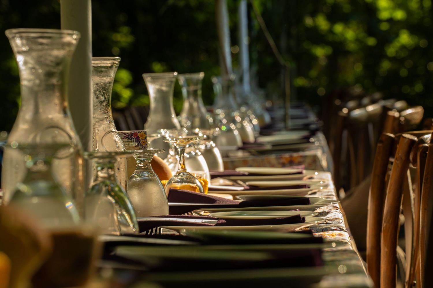 Close-up of a formal outdoor dinner table with glass carafes, plates, and golden evening light.