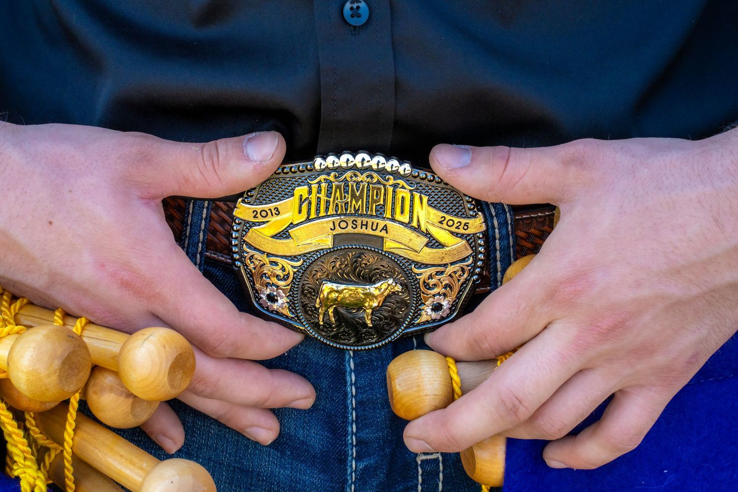 Close-up of a Champion belt buckle with cow engraving held by a person in a black shirt.