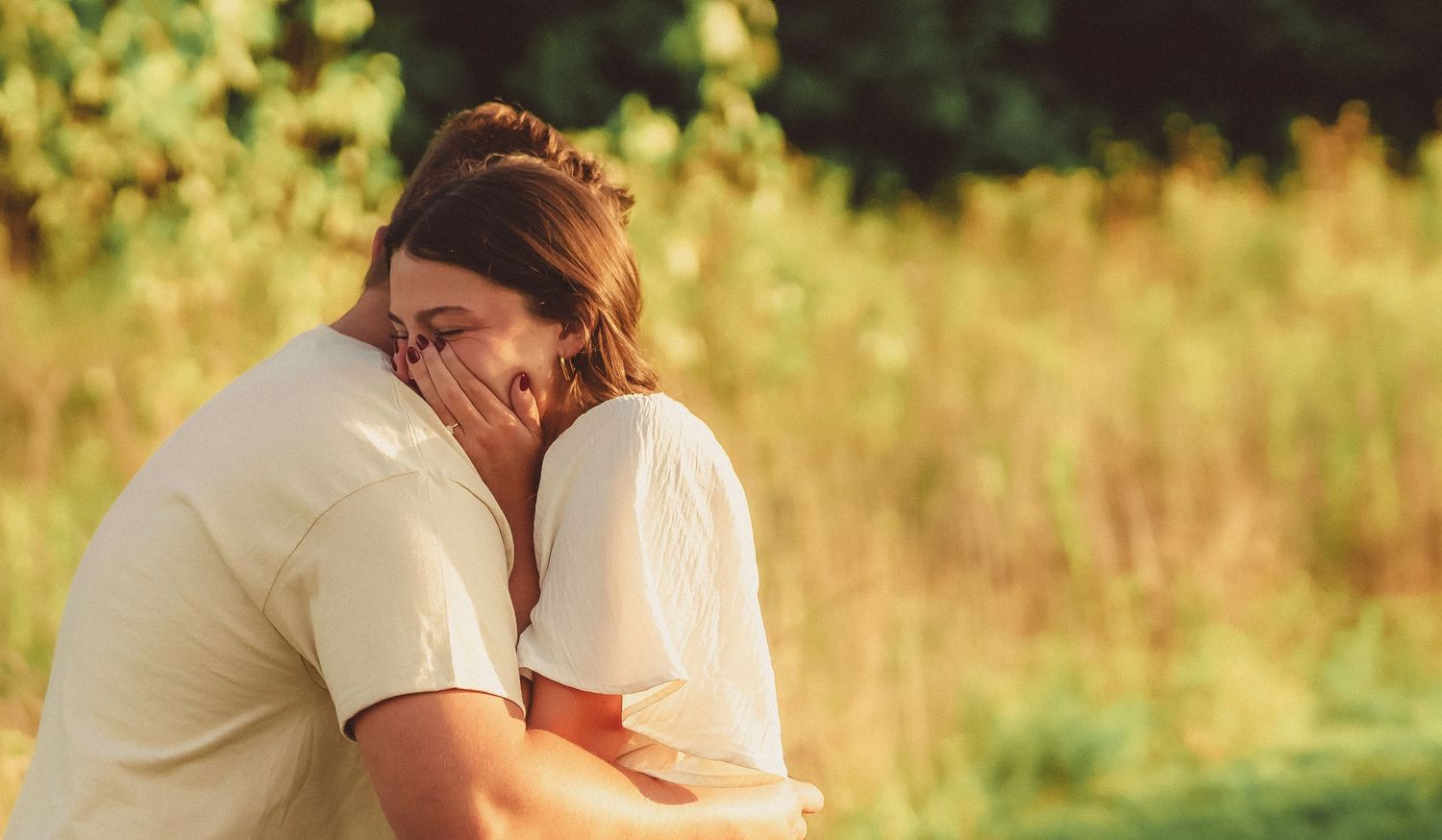 Emotional woman covering her face while being embraced by man after marriage proposal outdoors.