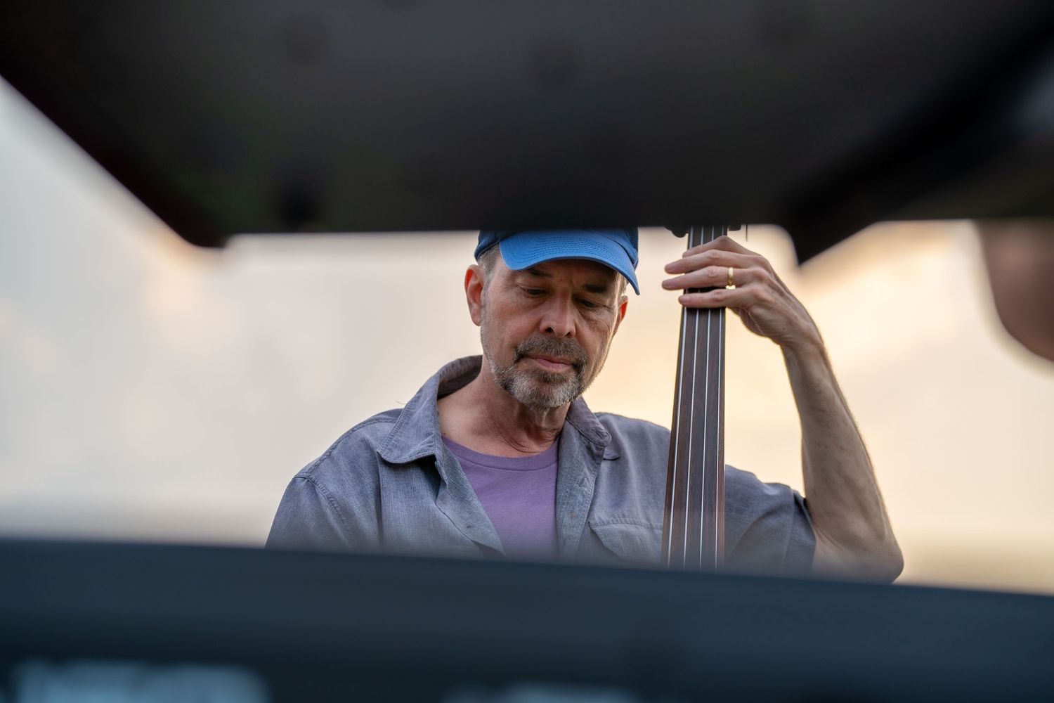 Older musician playing upright double bass outdoors at sunset concert.