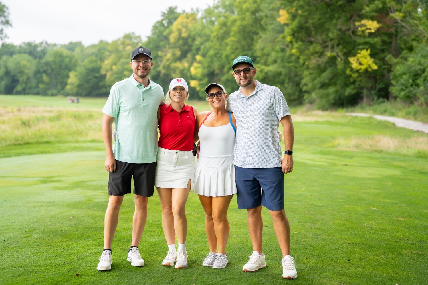 Four golfers smiling together on a lush green golf course on a sunny day.