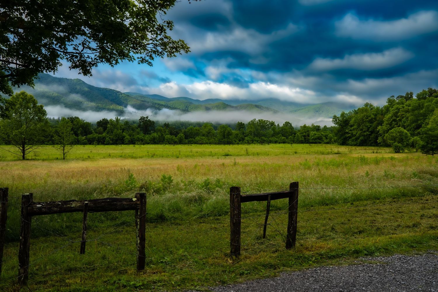 A wooden fence frames a green meadow with fog-covered mountains beyond.