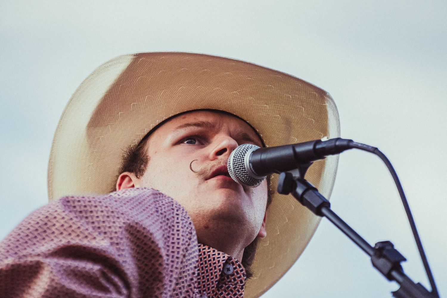 Man in cowboy hat singing into microphone at outdoor concert.