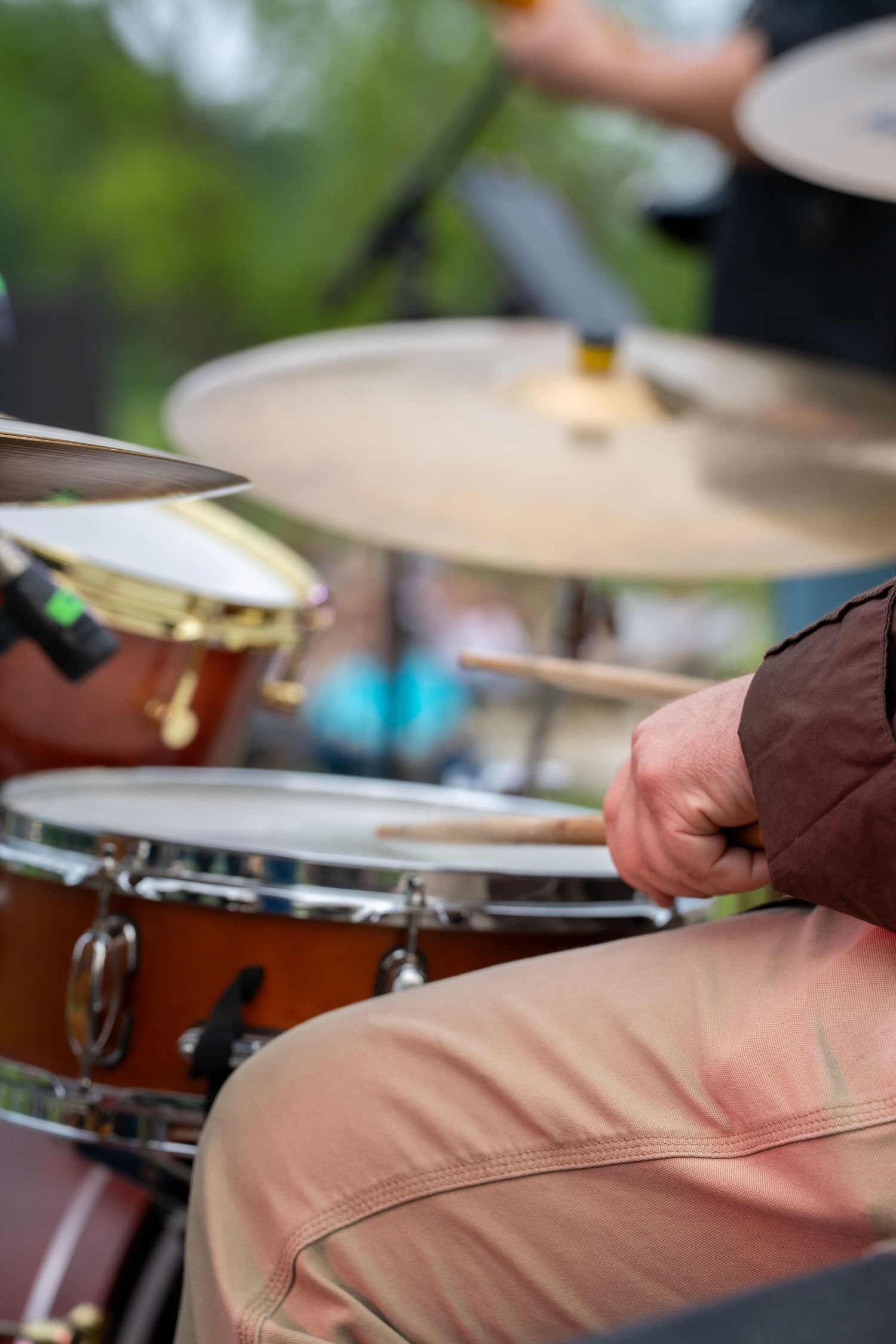 Close-up of drummer's hands playing snare drum with wooden drumsticks at an outdoor music performance.