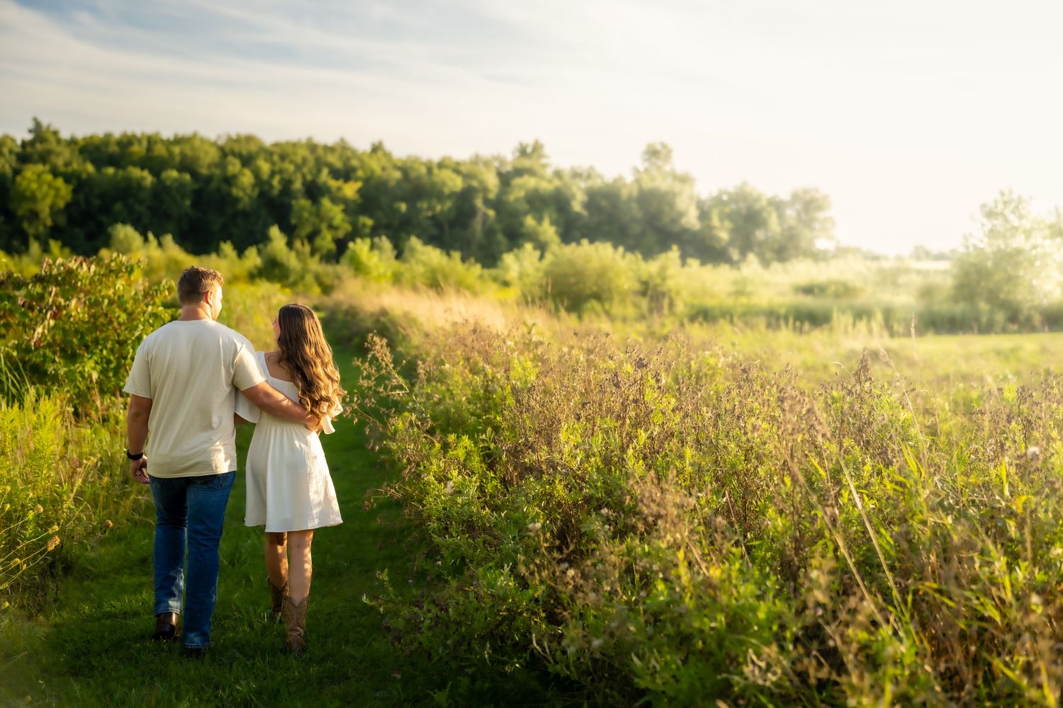Couple walking hand in hand through a scenic green meadow at sunset with wildflowers.