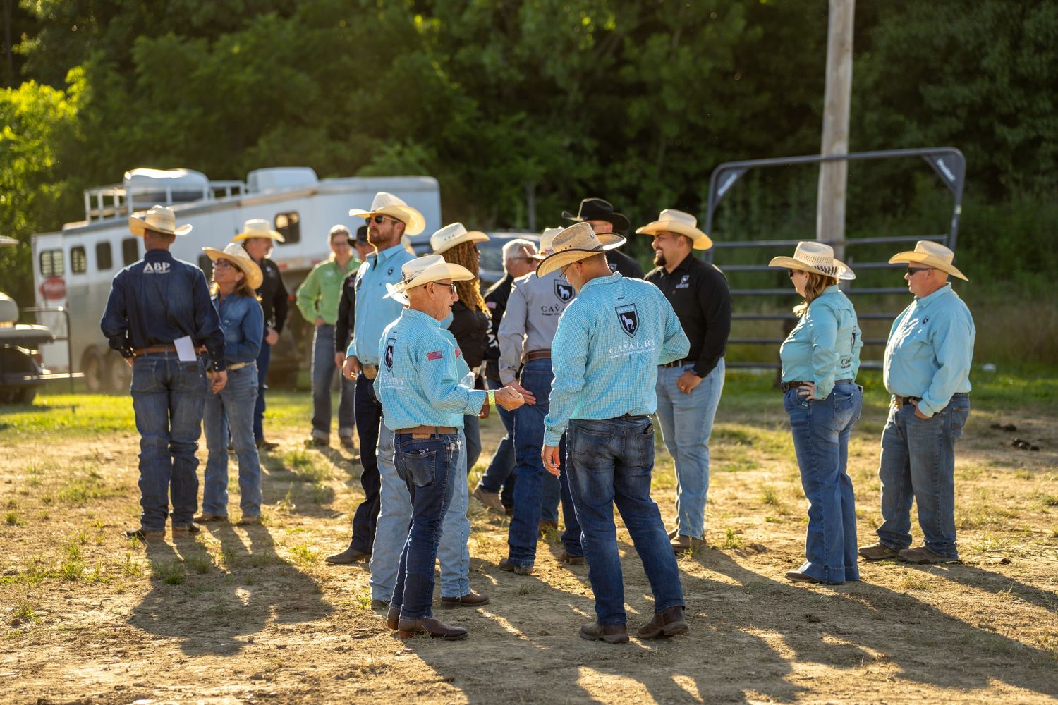 Cowboys and cowgirls in Western attire gather at a rodeo event, wearing cowboy hats and jeans in golden evening light.
