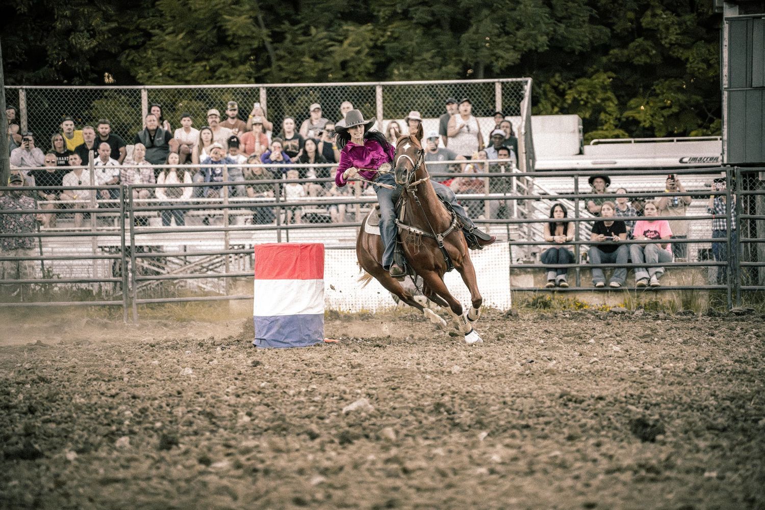 A rider on horseback races around a barrel during a rodeo competition with spectators watching.