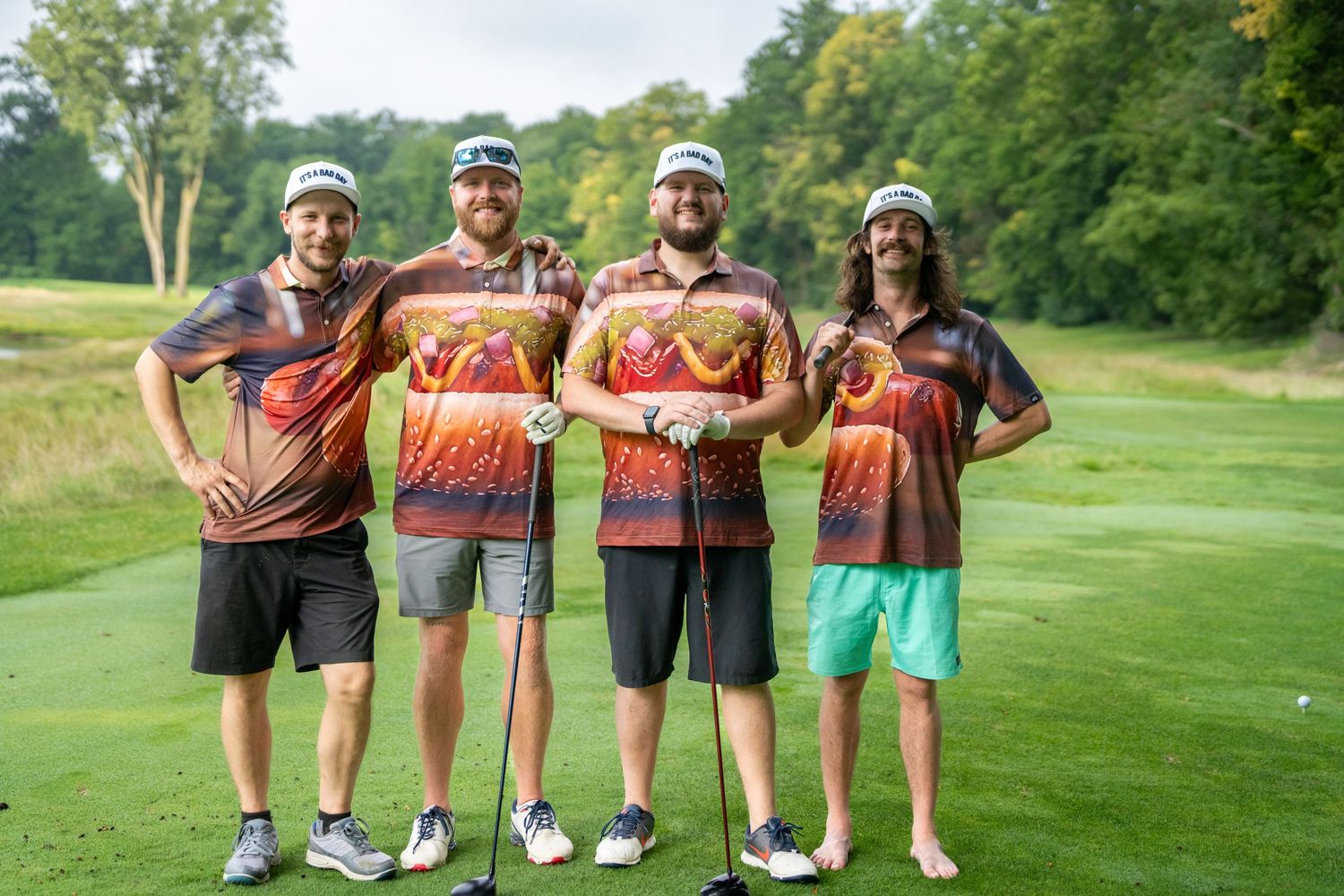 Four men in matching colorful golf jerseys posing together on a lush green golf course.