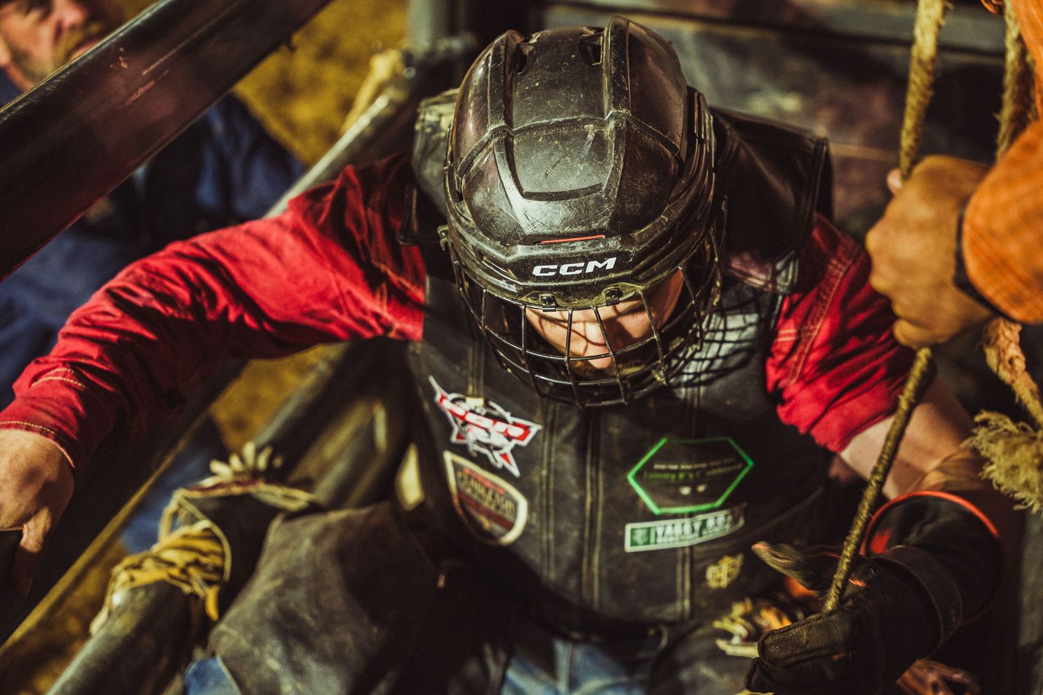 Bull rider in protective helmet and vest prepares in chute during rodeo competition.