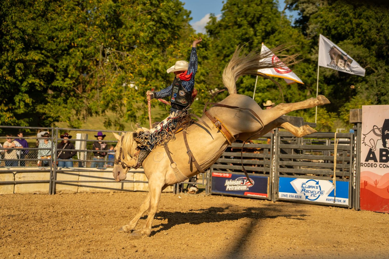 A rodeo rider holds on as a palomino horse bucks aggressively at an ABP Rodeo Company arena.