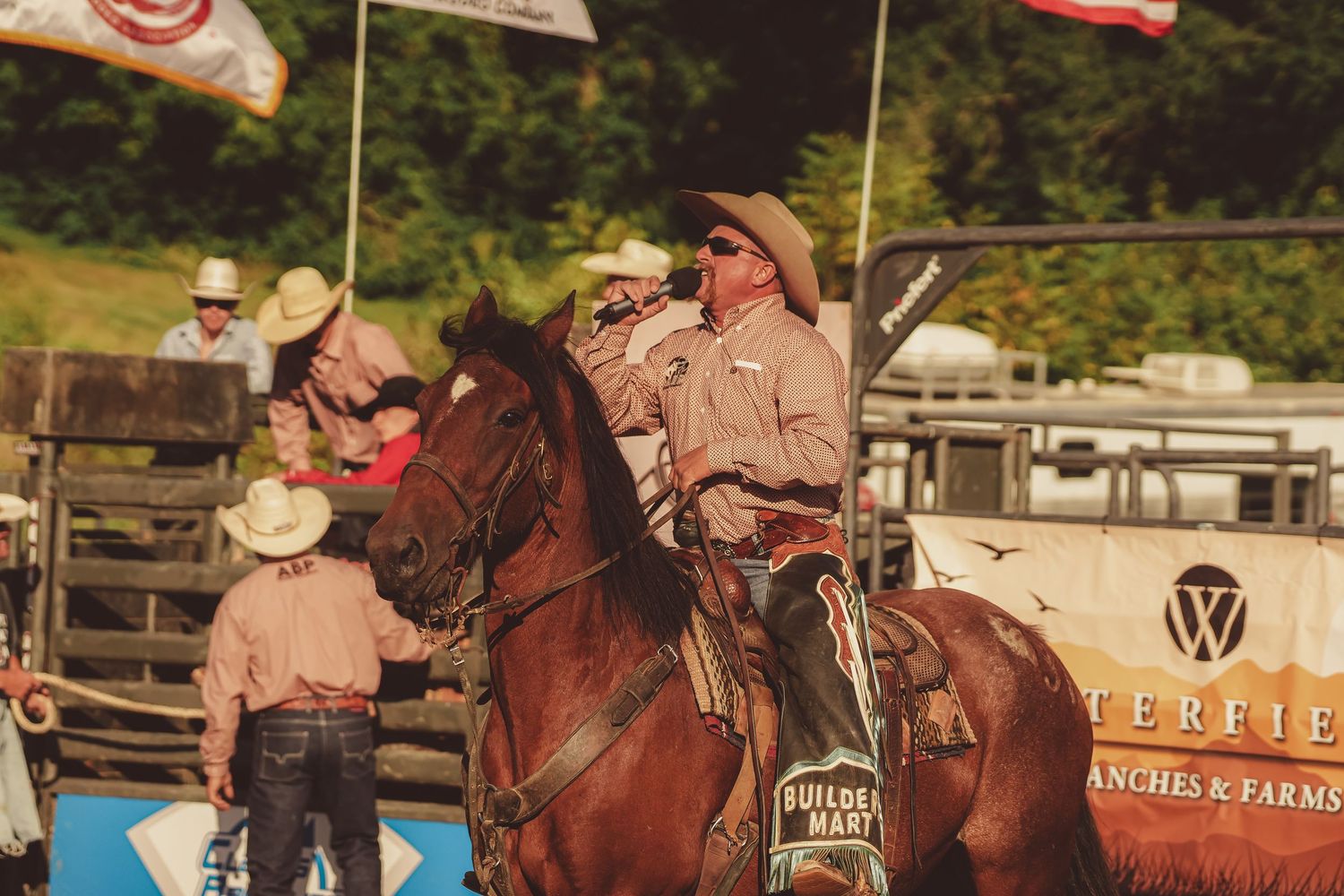 Cowboys on horseback gather near Waterfield Ranches Farms sponsor banner at a western rodeo event.