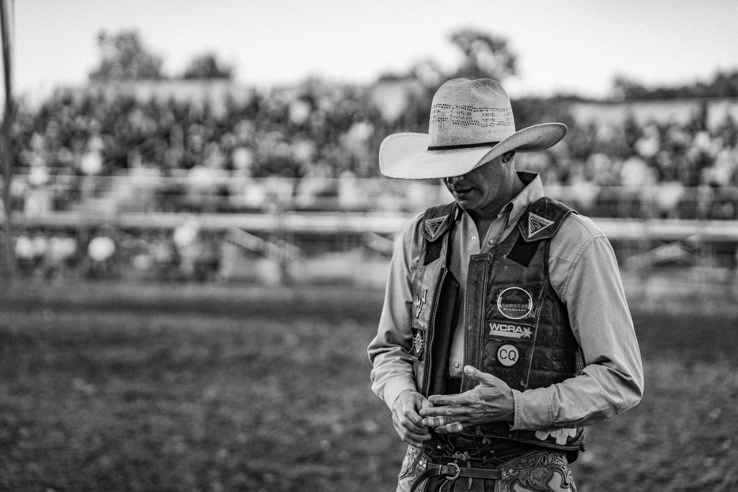 Black and white photo of a rodeo cowboy in a vest and cowboy hat standing in the arena.