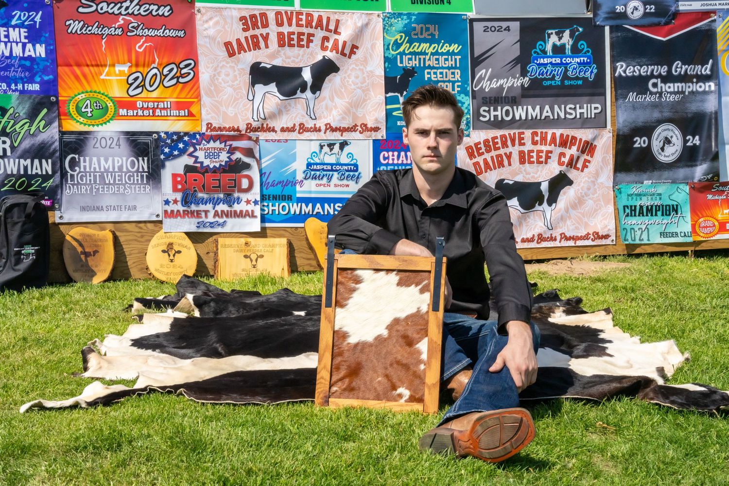 Young man sitting on cowhide rug surrounded by livestock show champion banners and awards.