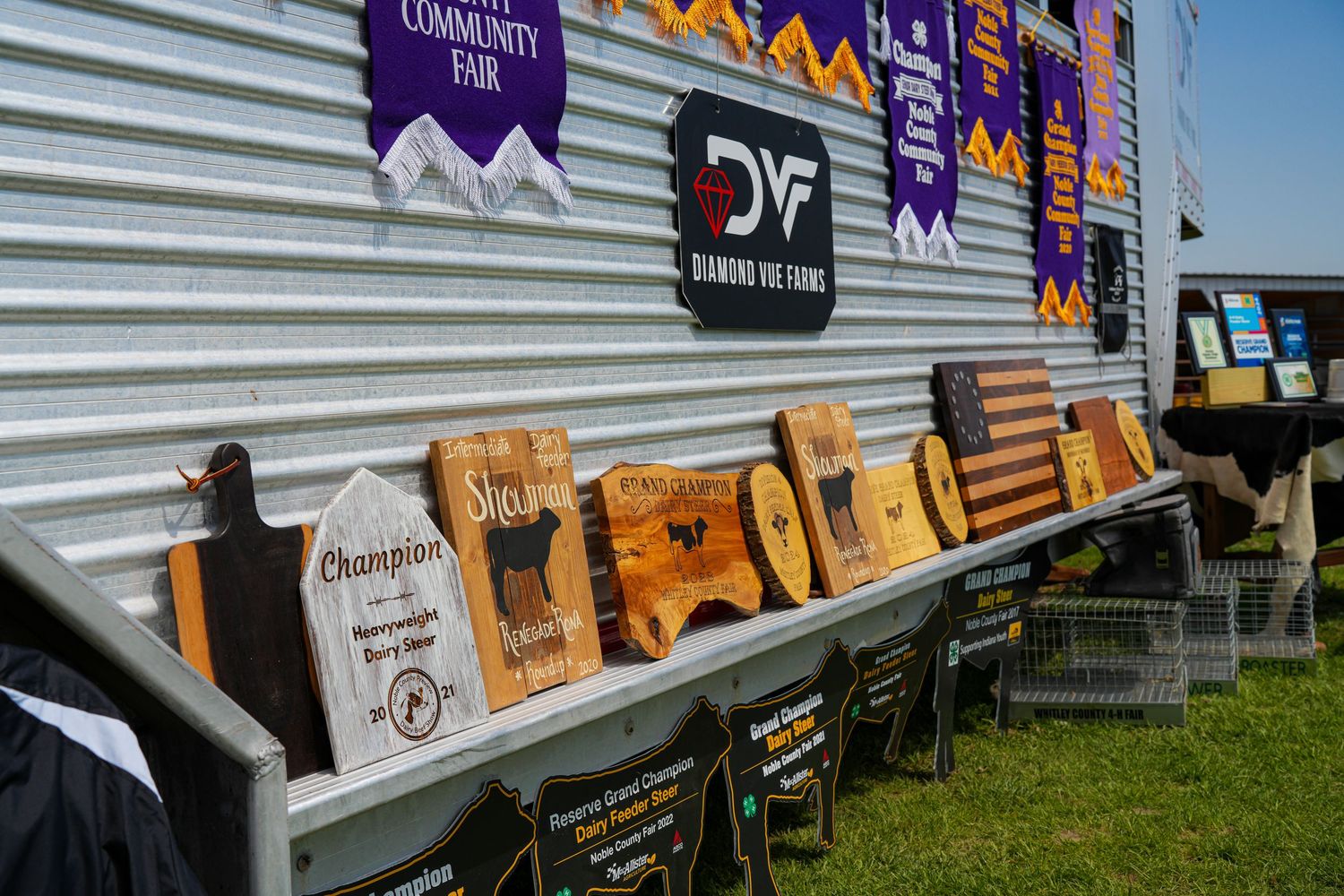 Wooden engraved champion plaques and awards displayed along a silver trailer at a fair.