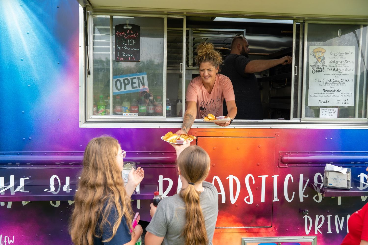 Food truck worker handing food to customers through a colorful open service window at an outdoor festival event.