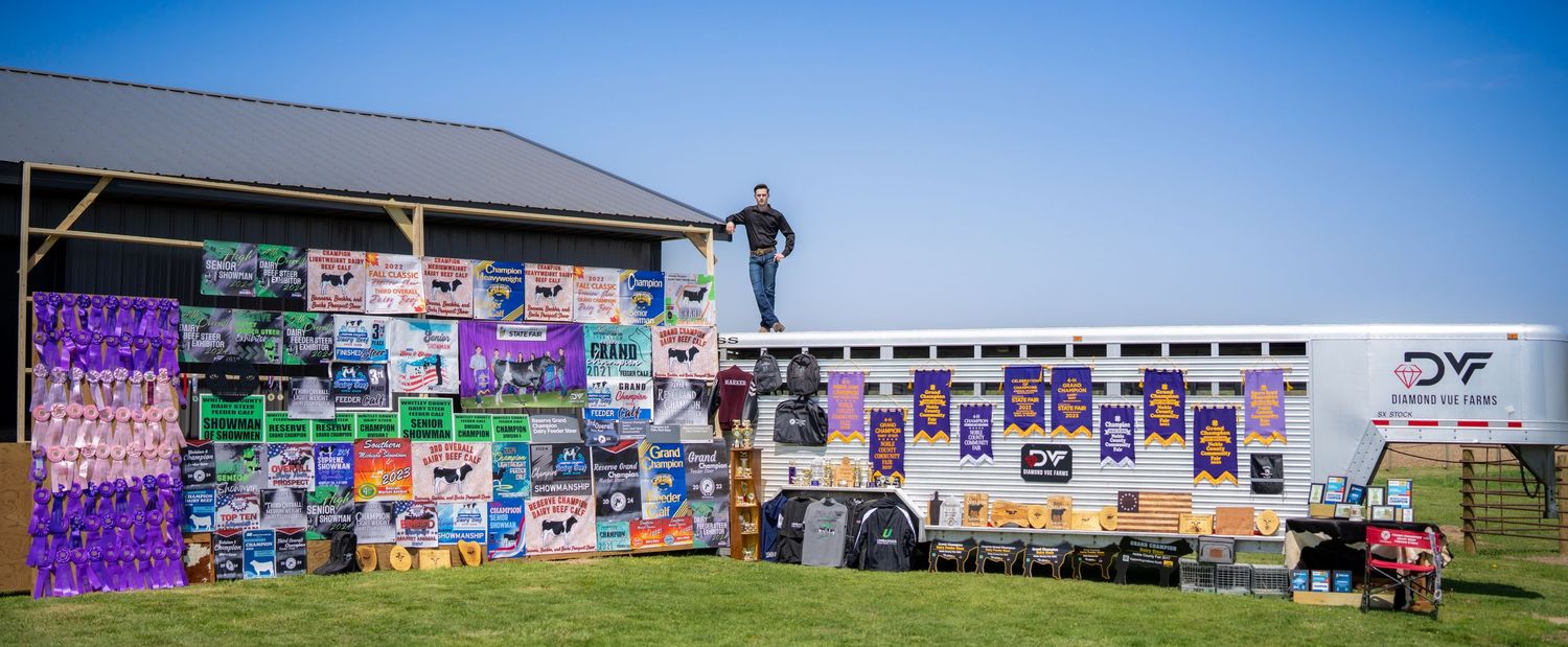 Person standing atop a trailer covered in colorful livestock show banners at a county fair.