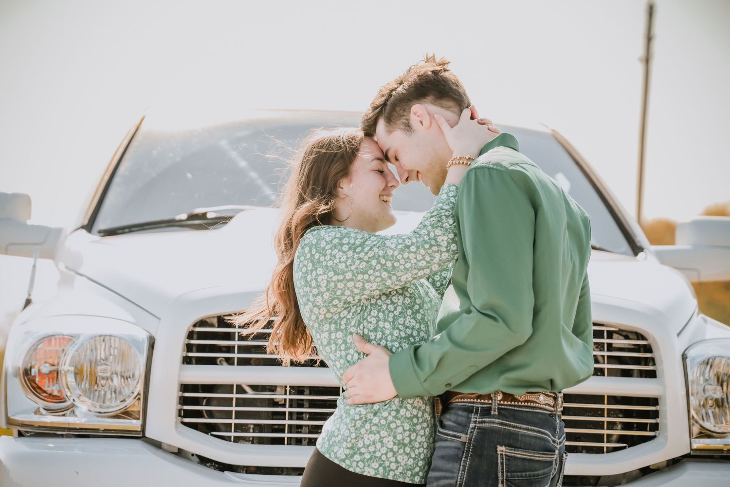 Young couple embracing and touching foreheads romantically in front of a white Dodge pickup truck outdoors.