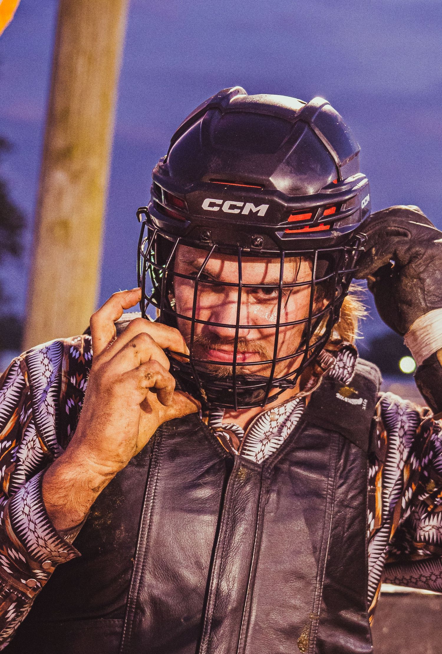 A rodeo athlete adjusts his CCM protective helmet and face guard before competing in a nighttime event.