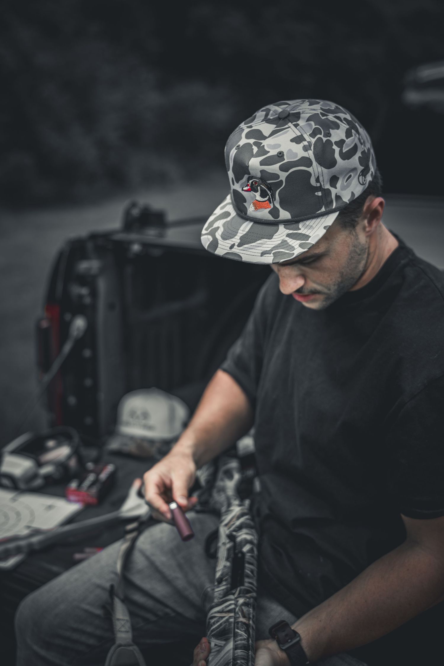 Man in camo snapback cap examining equipment near truck bed outdoors.