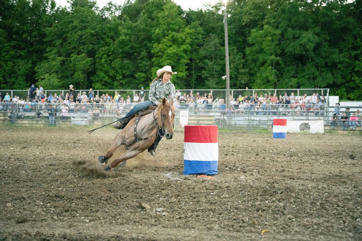 Cowgirl riding a horse around a barrel during a barrel racing event at a rodeo.