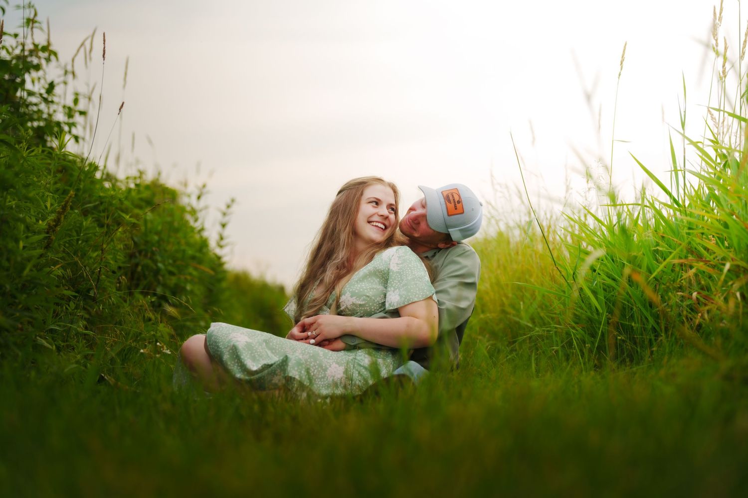 Joyful couple cuddling and laughing together while sitting in a lush green field.