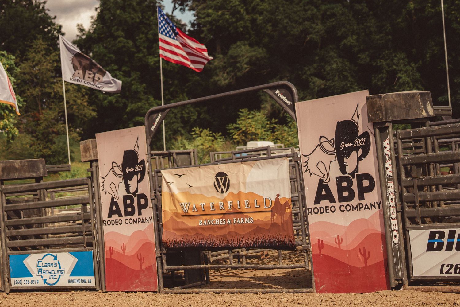 ABP Rodeo Company branded chute gate with American flag and Wrangler banner at outdoor rodeo event.