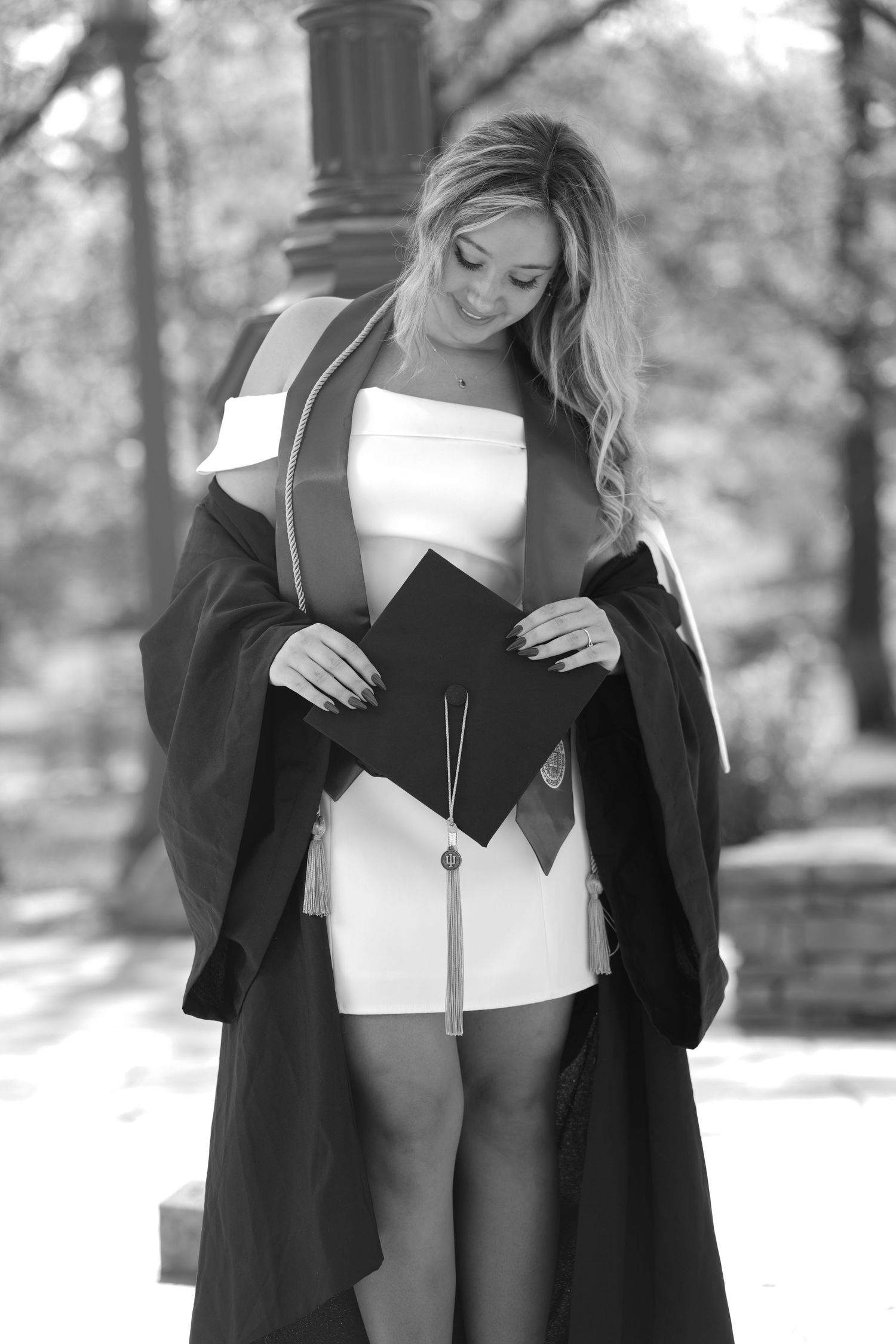 Young woman in graduation gown and cap posing outdoors in black and white photo.