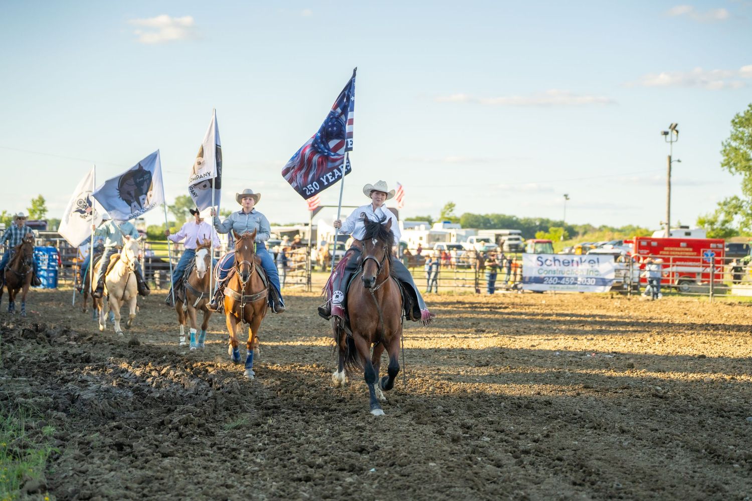 Horseback riders carrying flags parade through a dirt rodeo arena before a crowd.