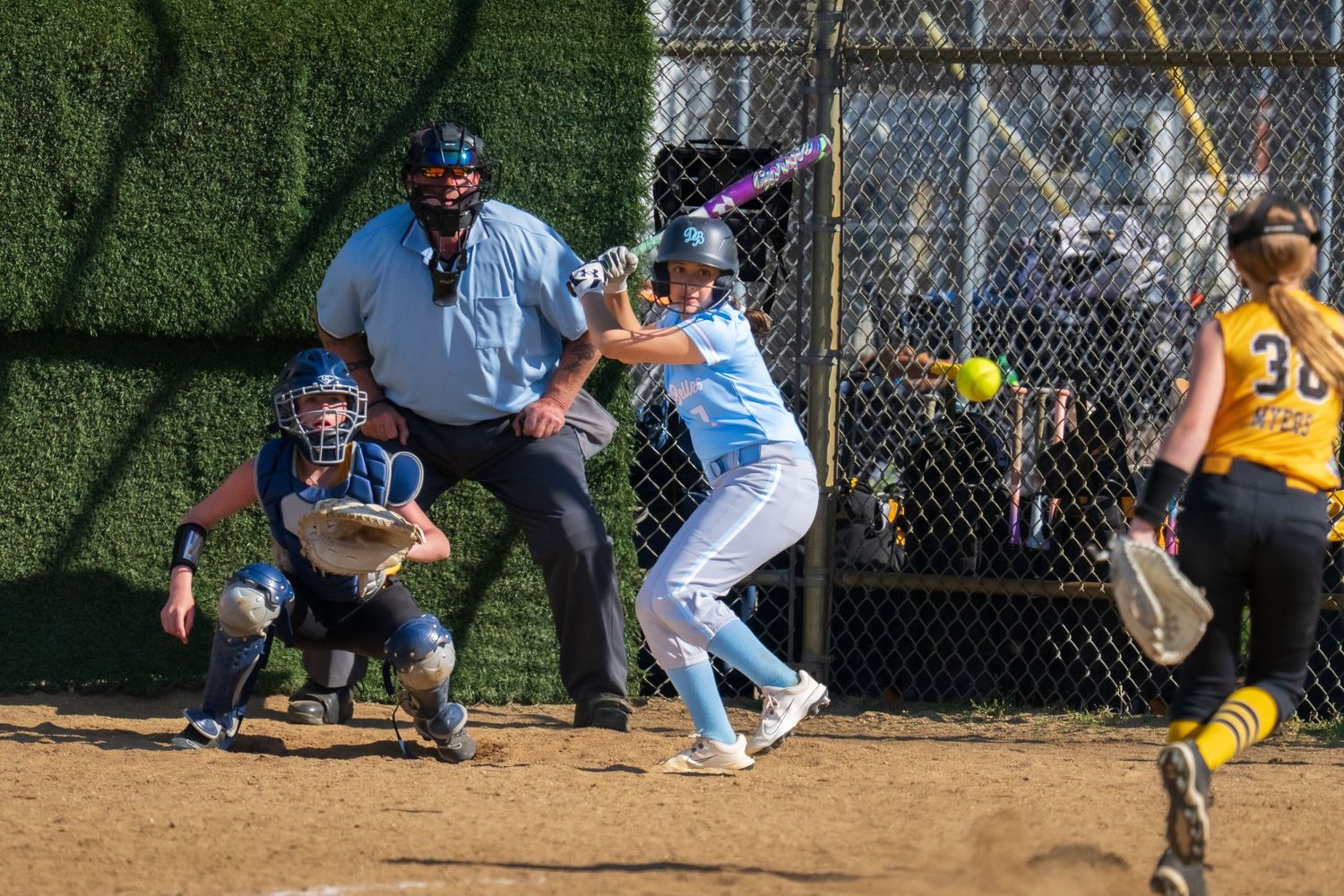 Softball batter swinging at pitch with catcher and umpire behind home plate during competitive game.