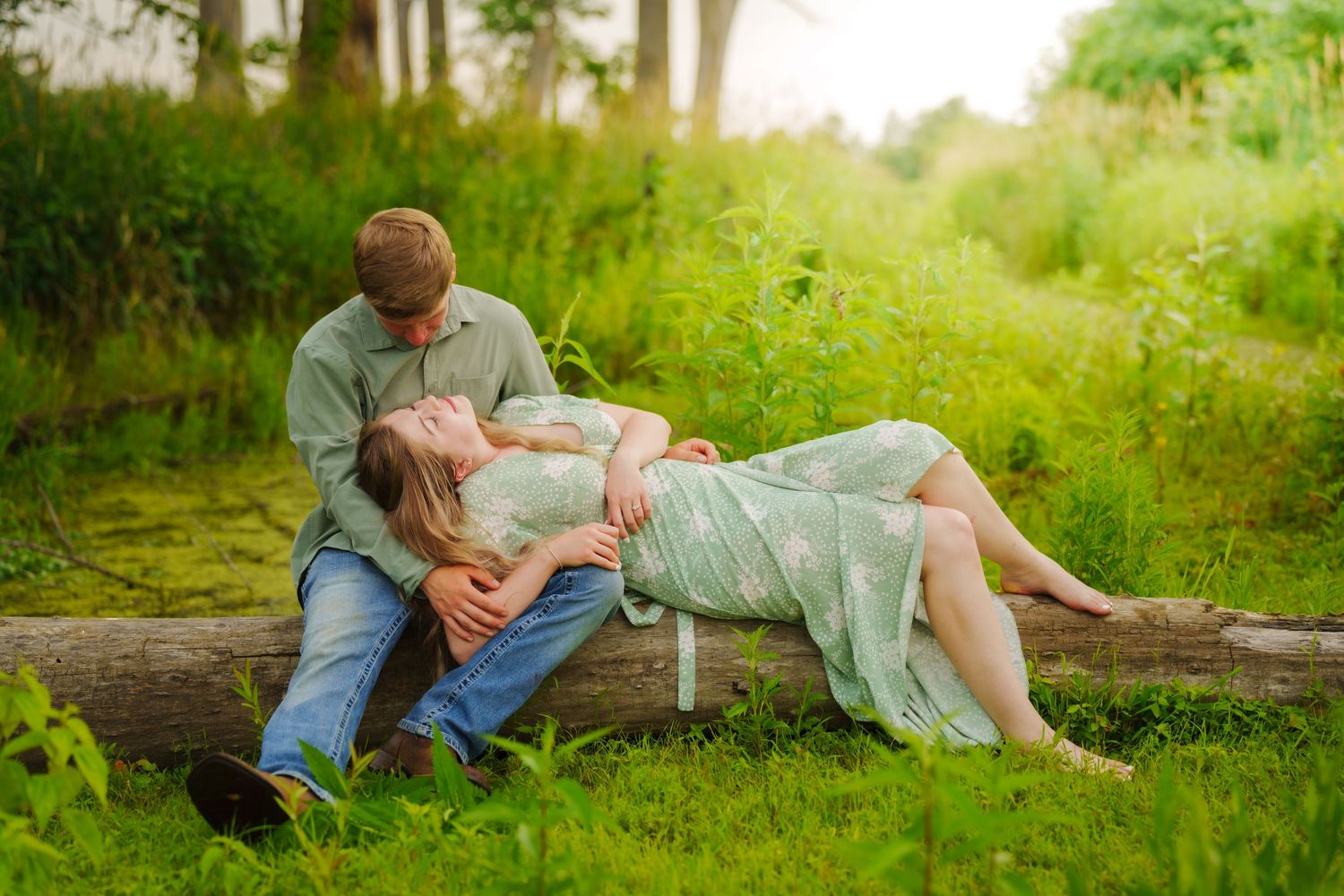 Romantic couple relaxing on a fallen log in a lush green outdoor setting.