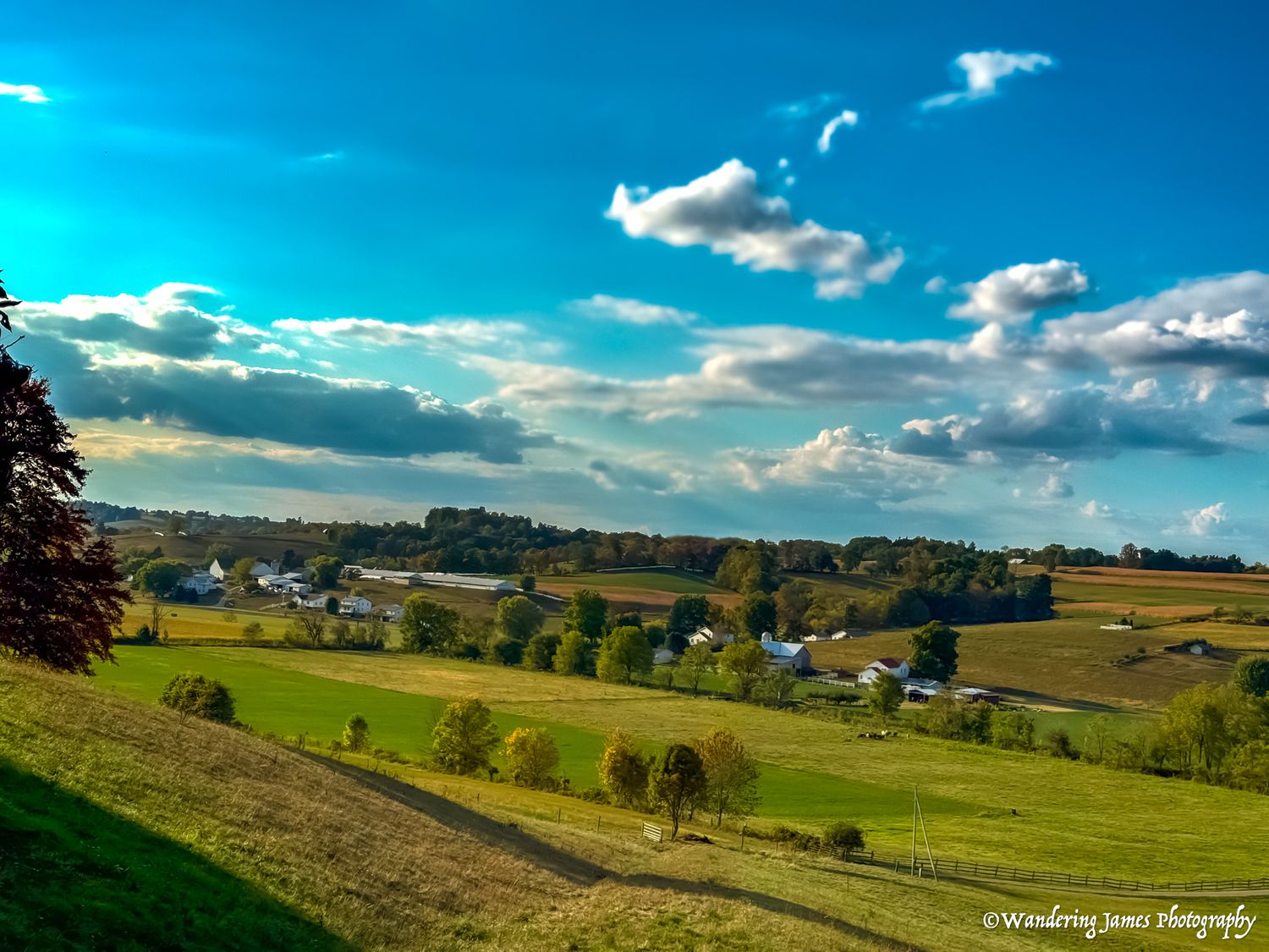 A scenic rural valley with farms and rolling green fields under a blue sky.