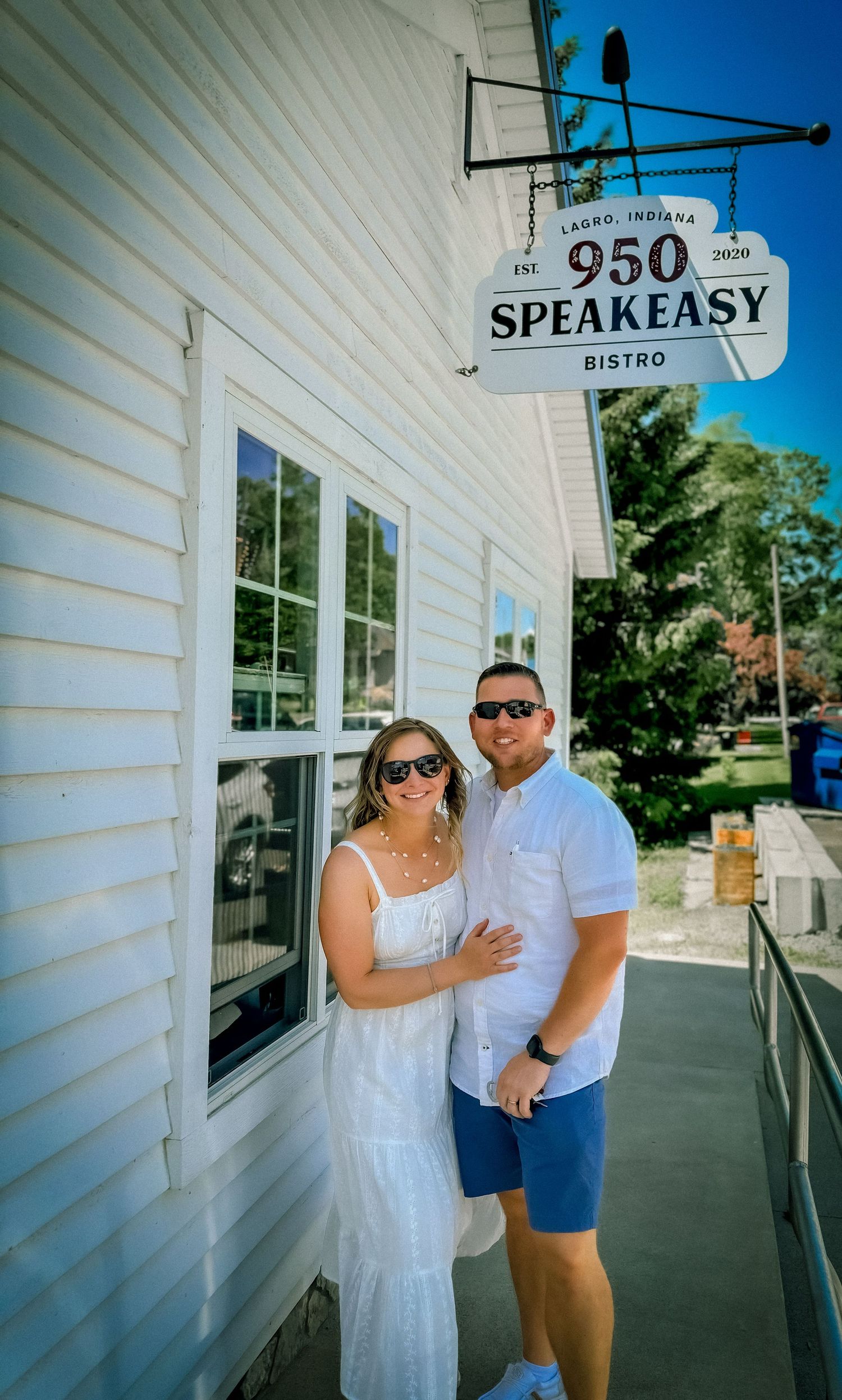 Couple in white outfits posing outside the 950 Speakeasy Bistro in Lagro, Indiana on a sunny day.