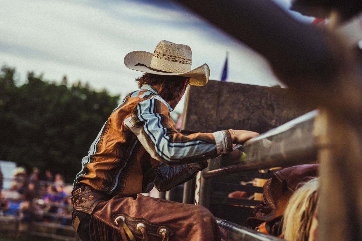 A cowboy in a hat and fringed chaps prepares to ride at a rodeo event.