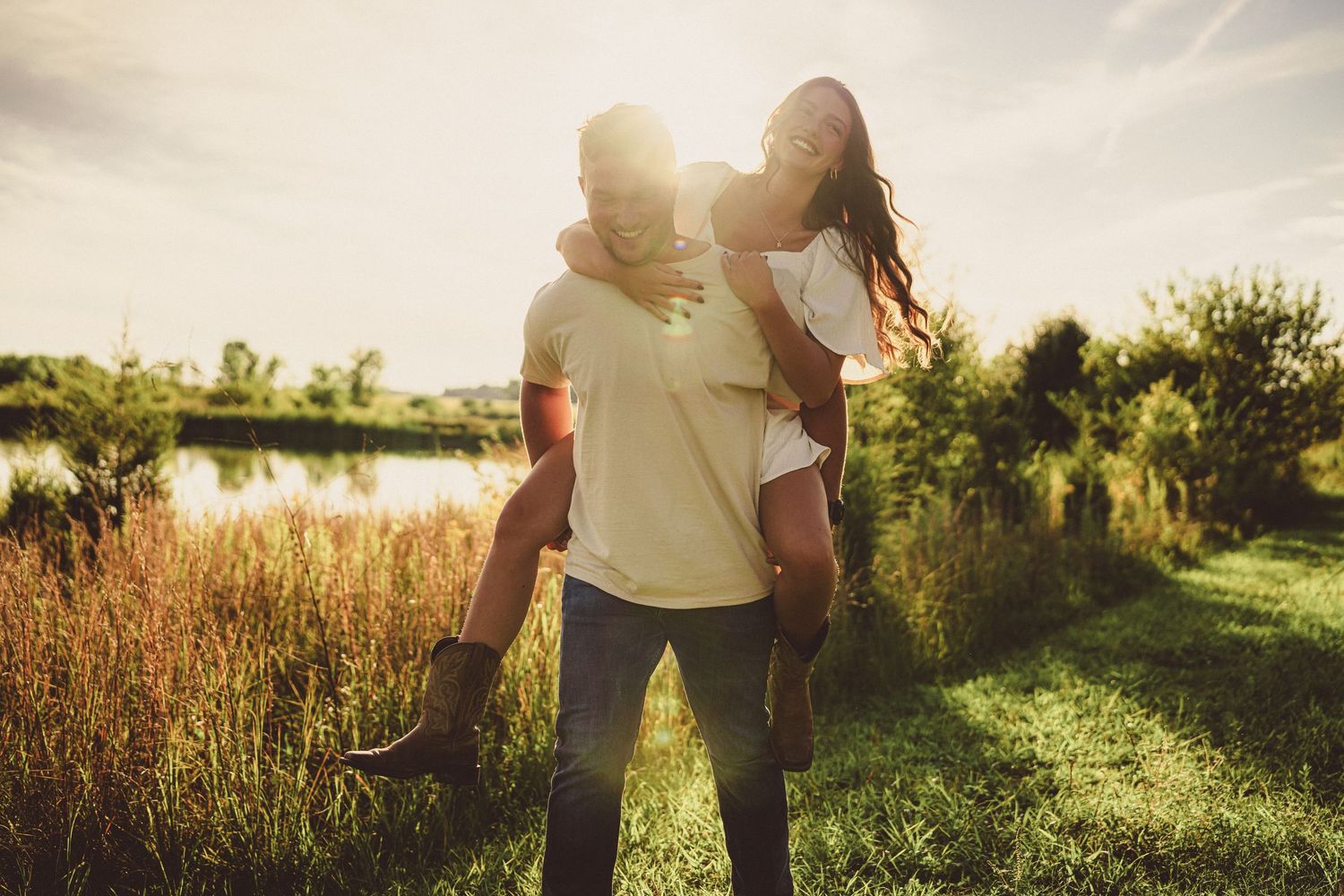 Couple shares a joyful piggyback ride in golden sunset light near a serene pond.