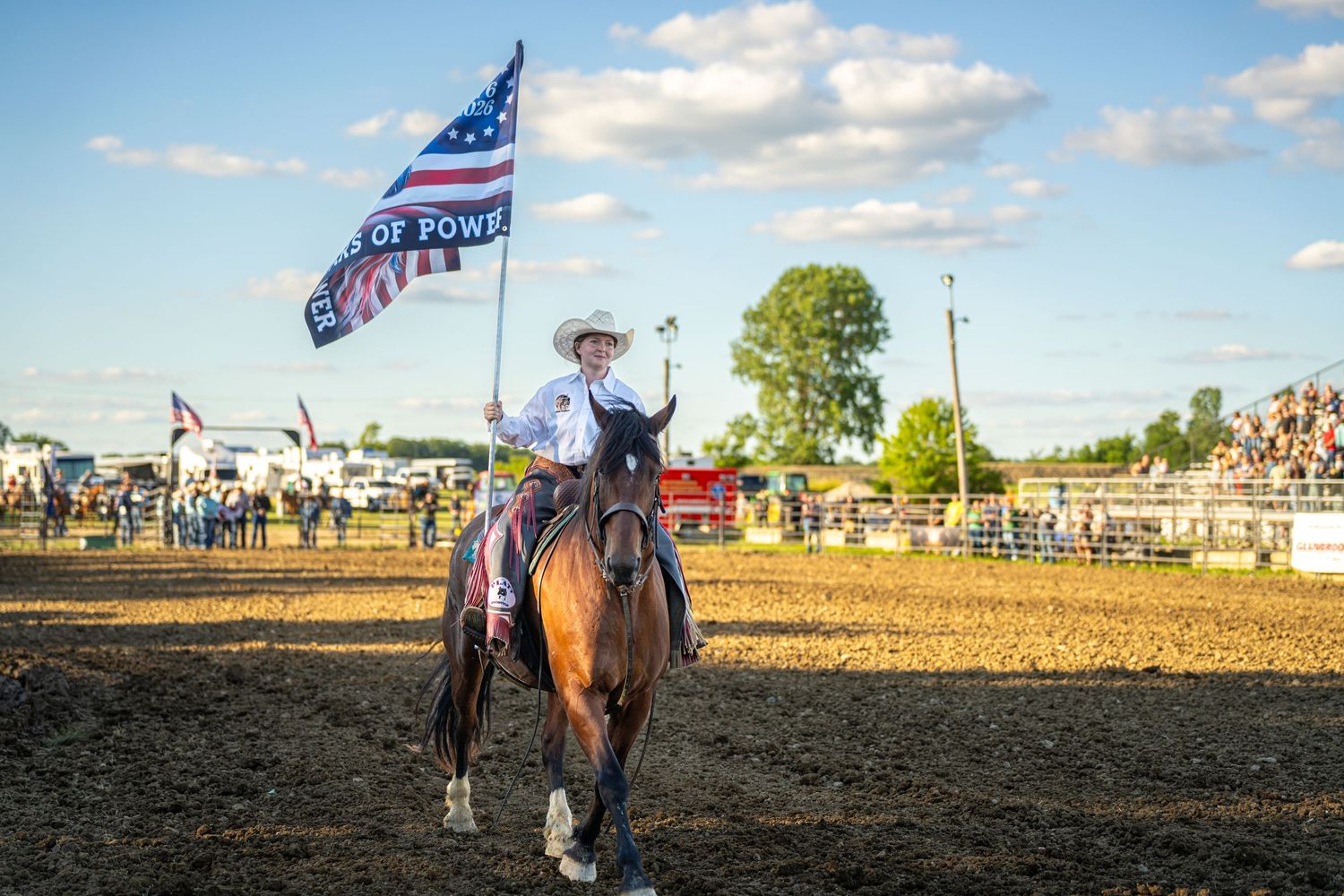 A rider on horseback carries an American flag across a dirt rodeo arena during an opening ceremony.