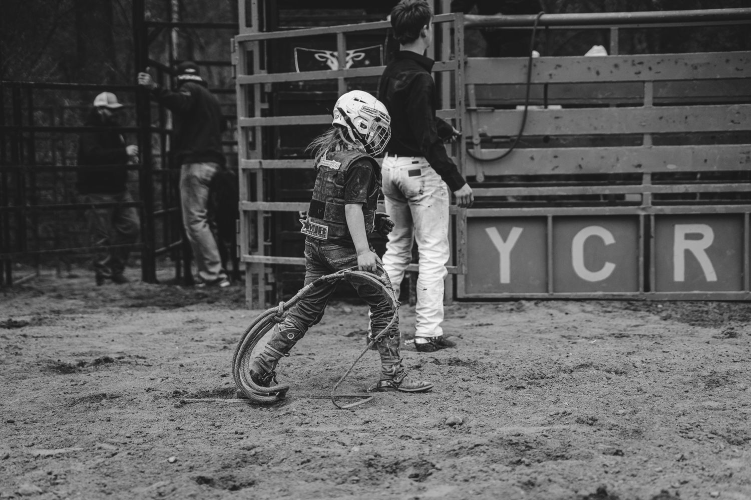 Young rodeo clown in helmet rolling tire in sandy arena at YCR rodeo event.