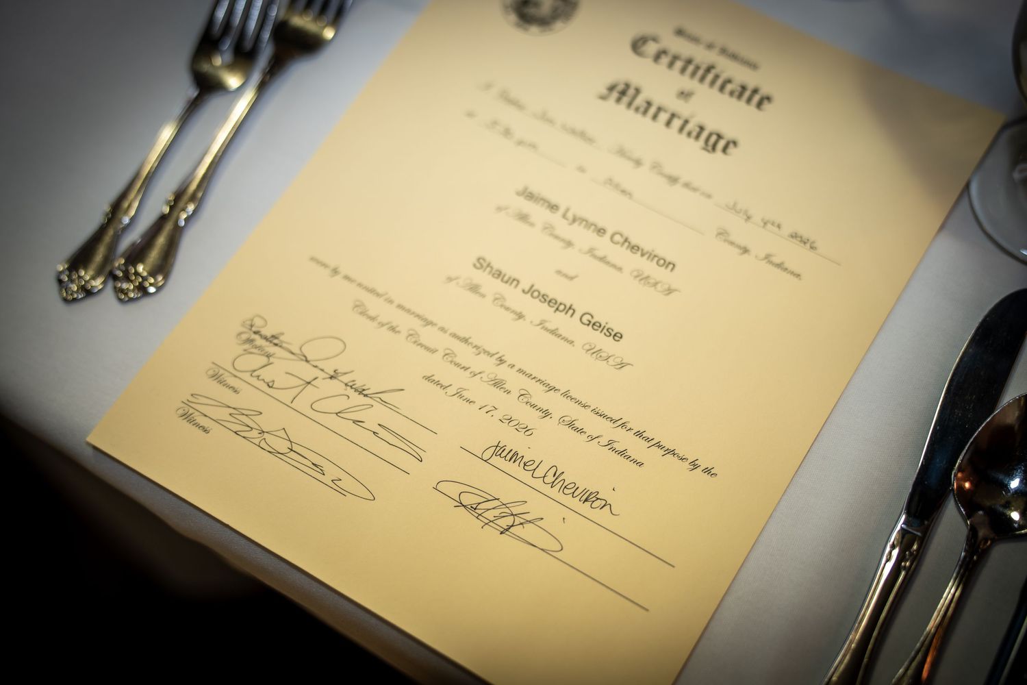 Gold marriage certificate on white tablecloth with silverware, official wedding document with signatures.
