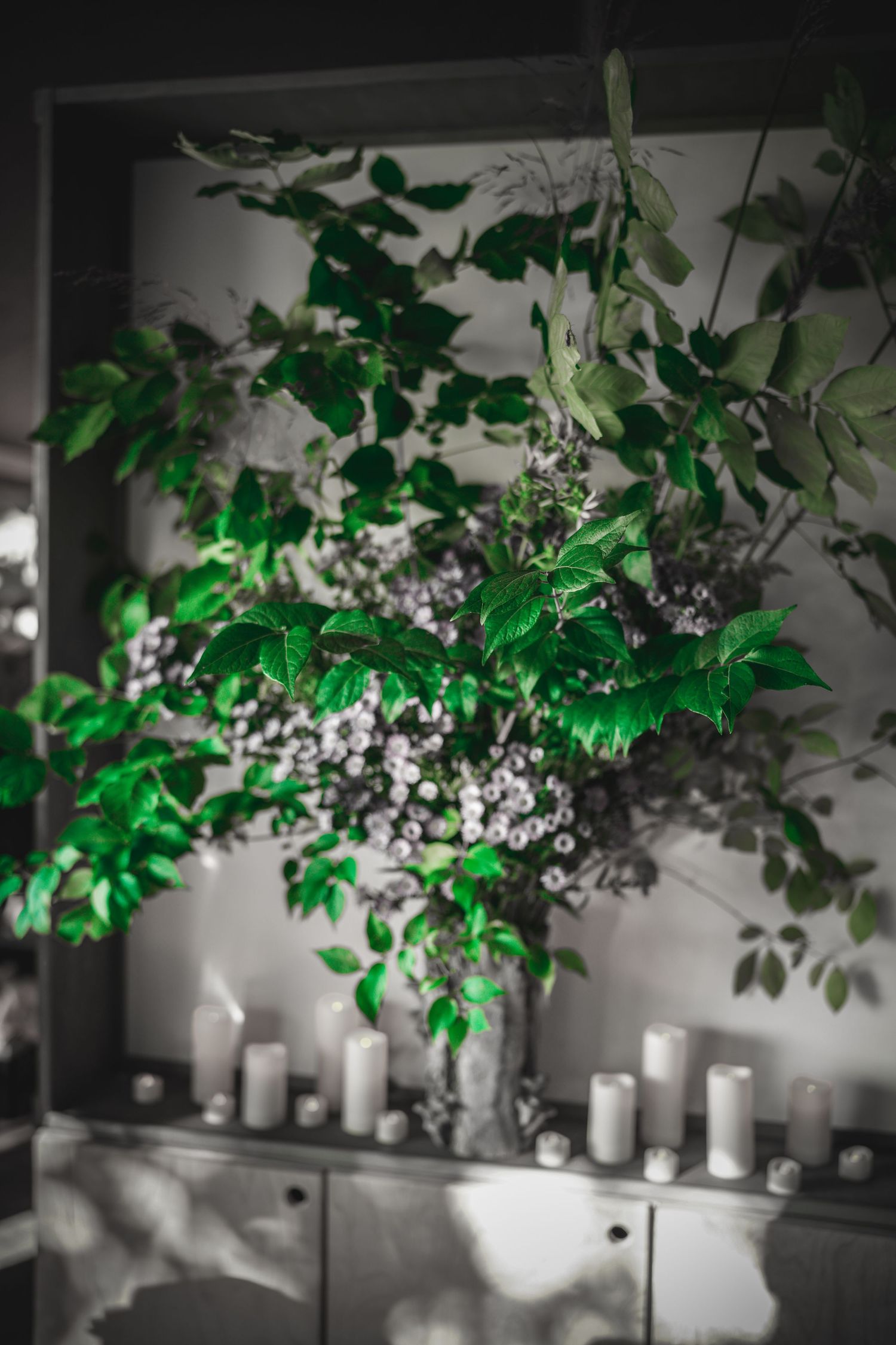Dramatic floral arrangement with green leaves and white berries surrounded by white pillar candles.
