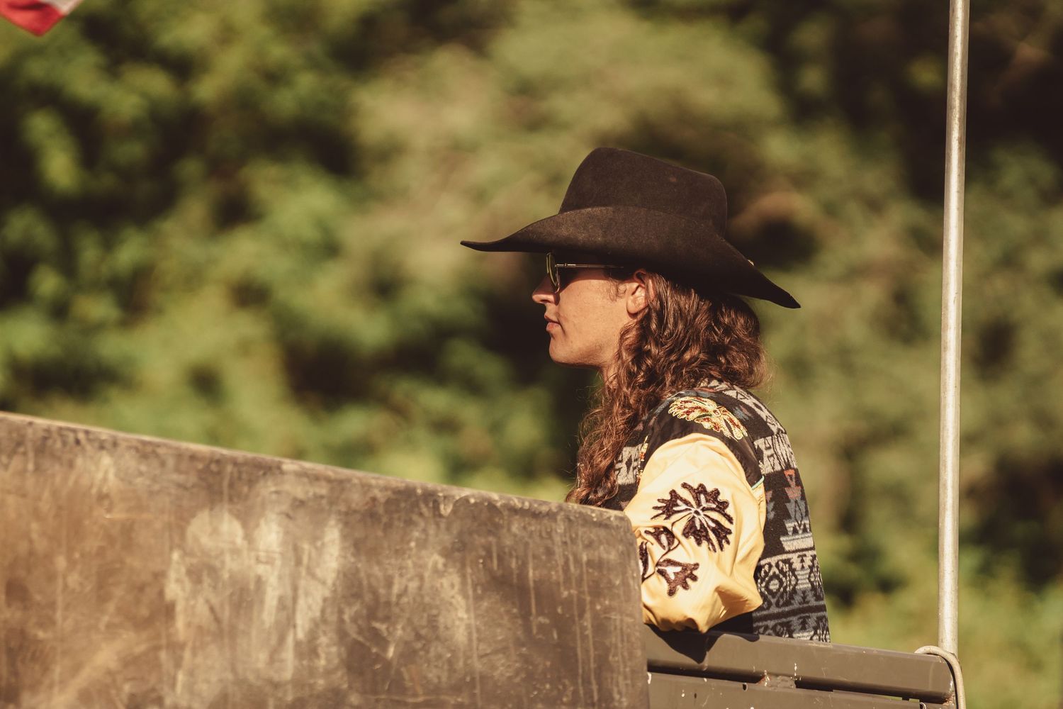 Side profile of a woman wearing a dark cowboy hat and patterned sweater at an outdoor country event.